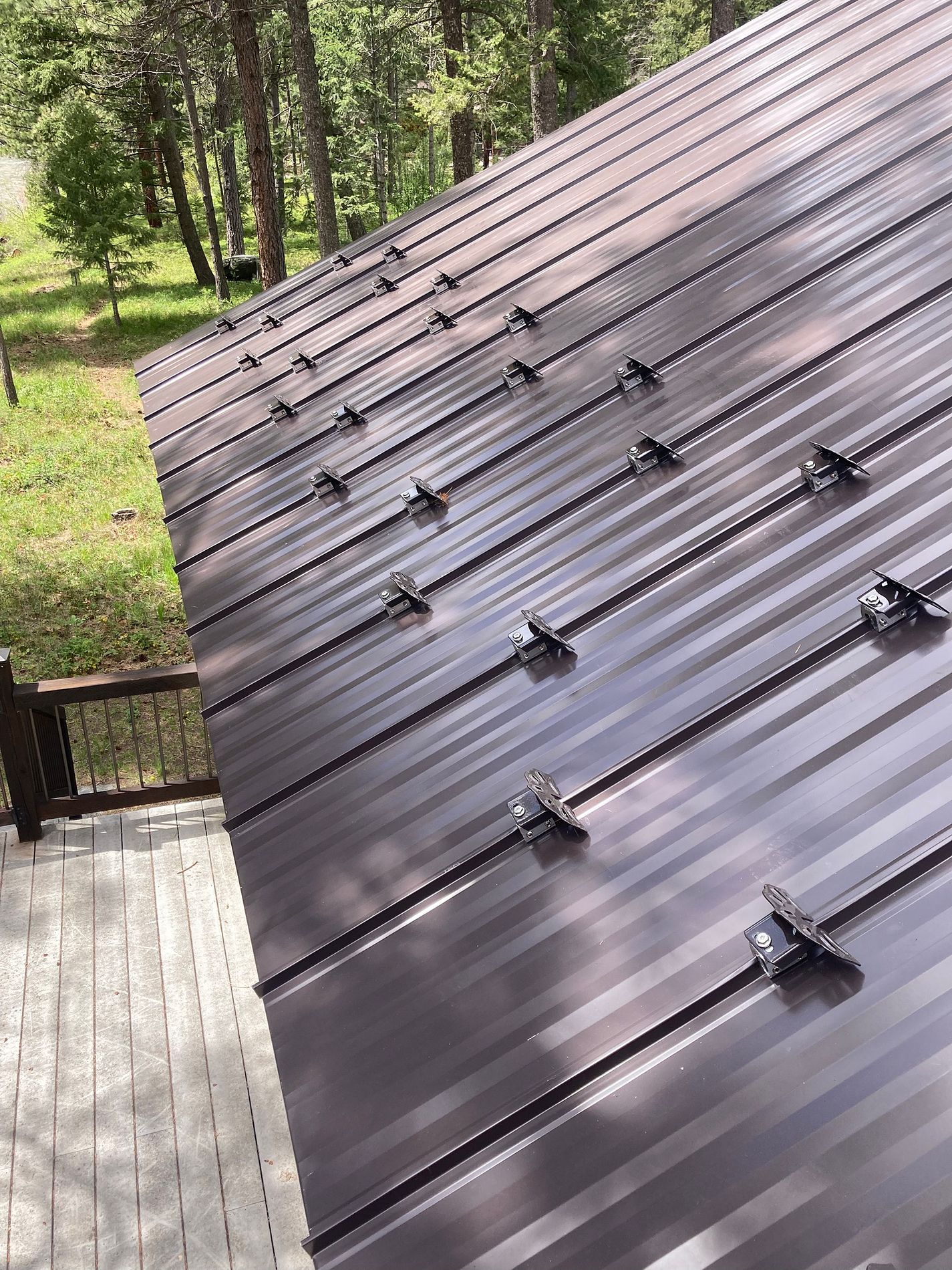 Close-up of a brown standing-seam metal roof fitted with rows of snow guards, trees behind.