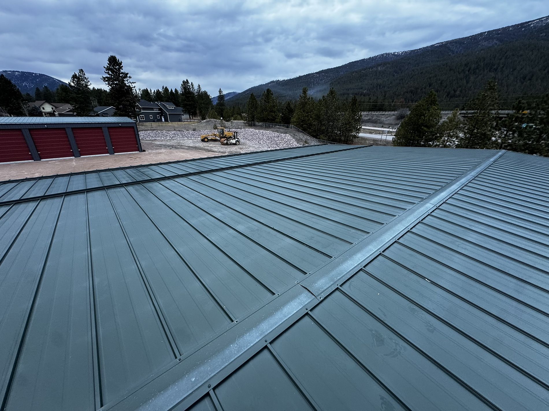 Green standing-seam metal roof seen along its panels with red roof vents and mountains.