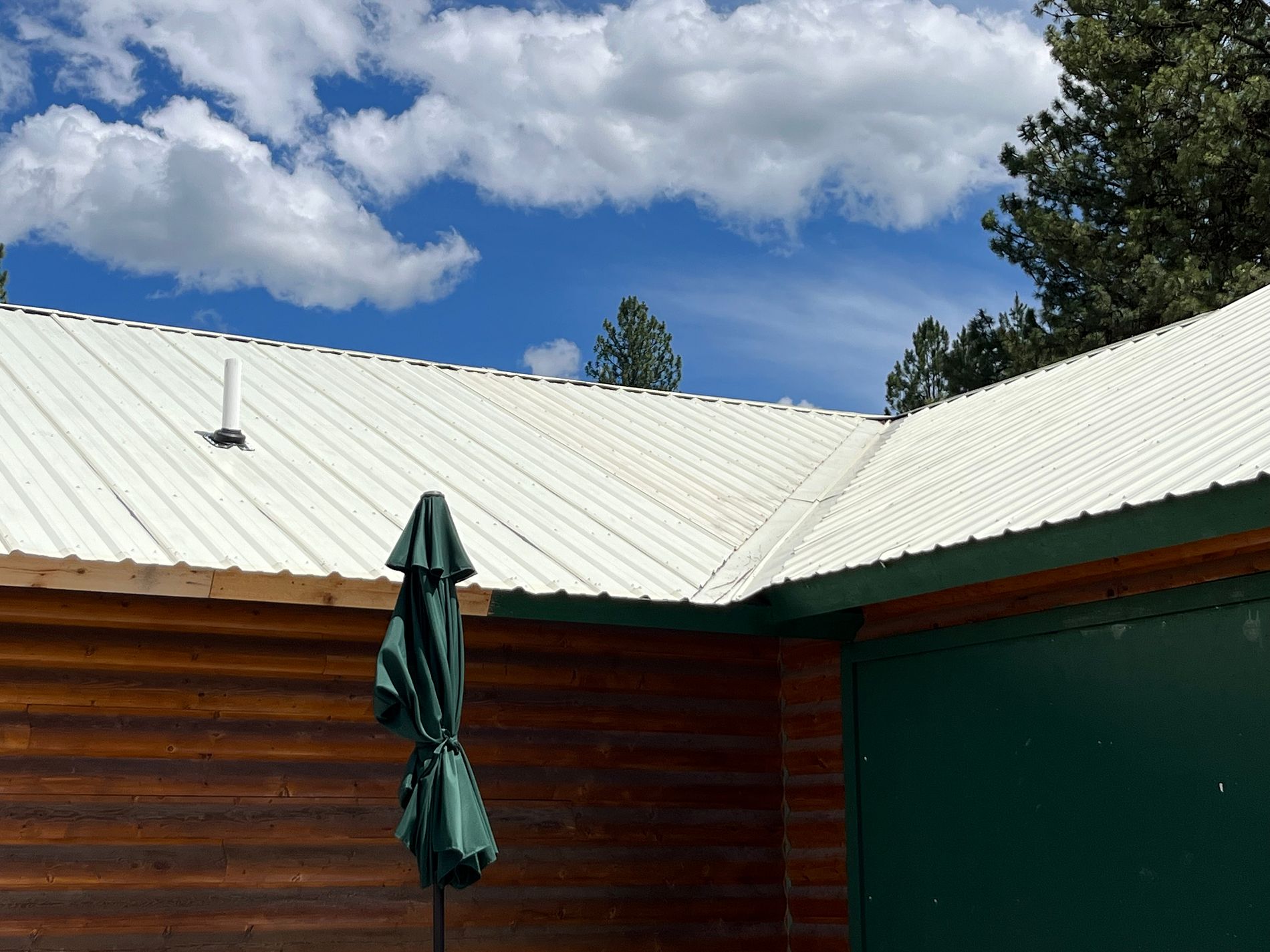 Log cabin home with a cream-colored metal roof and a green patio umbrella.