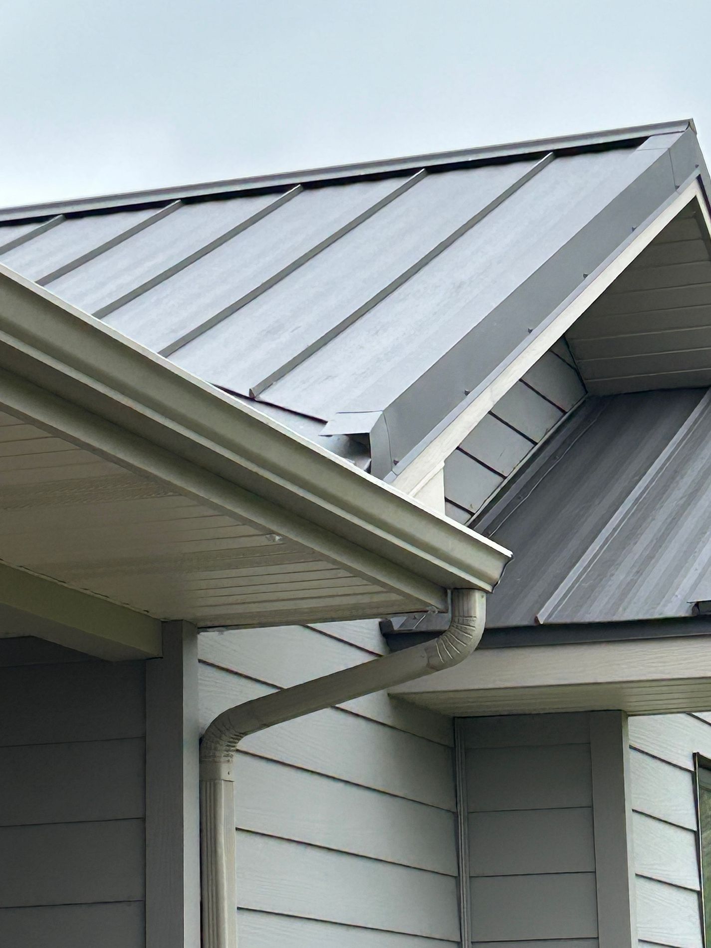 Detail of a standing-seam metal roof meeting a seamless gutter and downspout, cleanly flashed