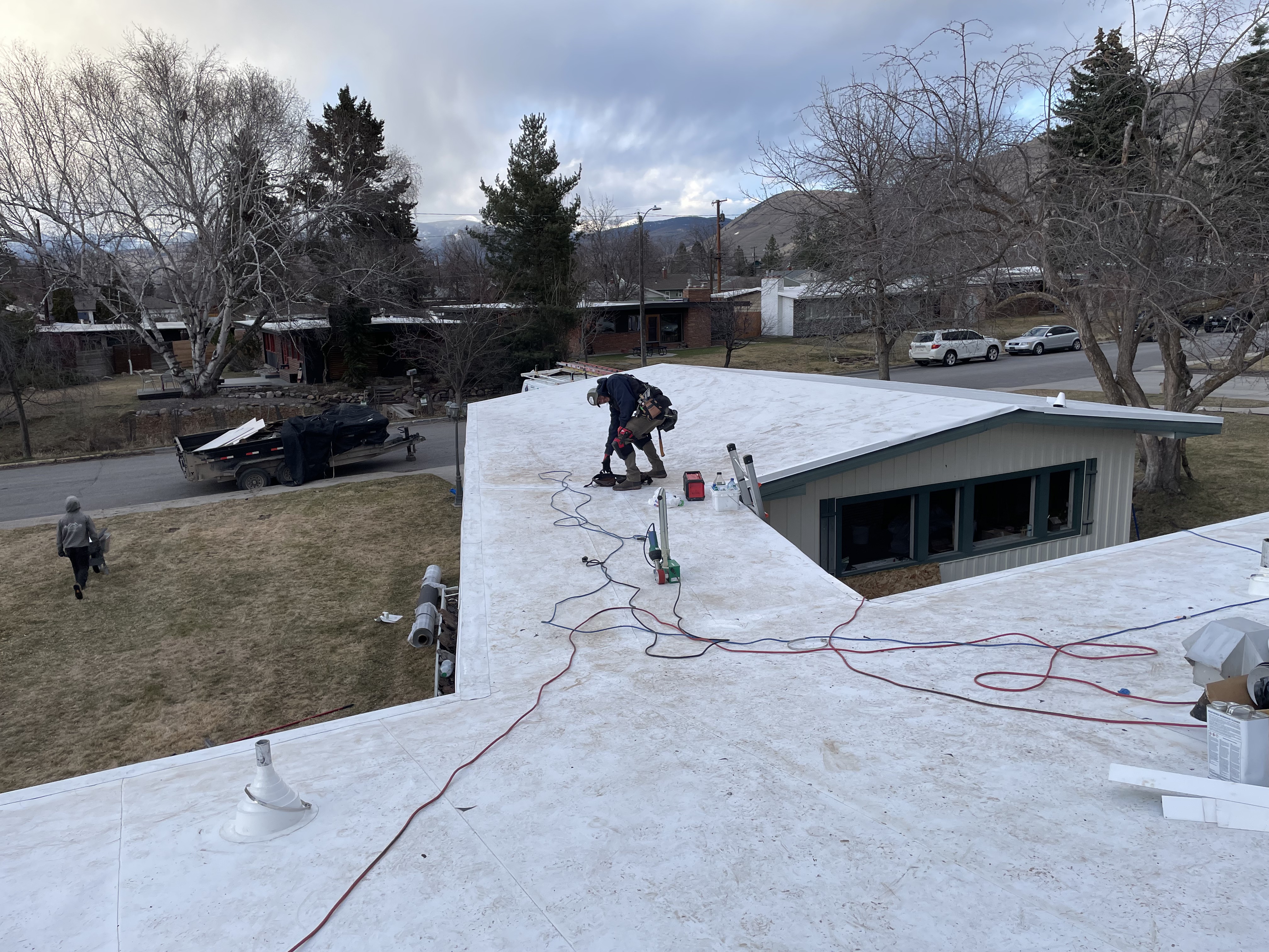 Low-slope roof covered in white underlayment during a reroof, a worker on the deck of a ranch home.