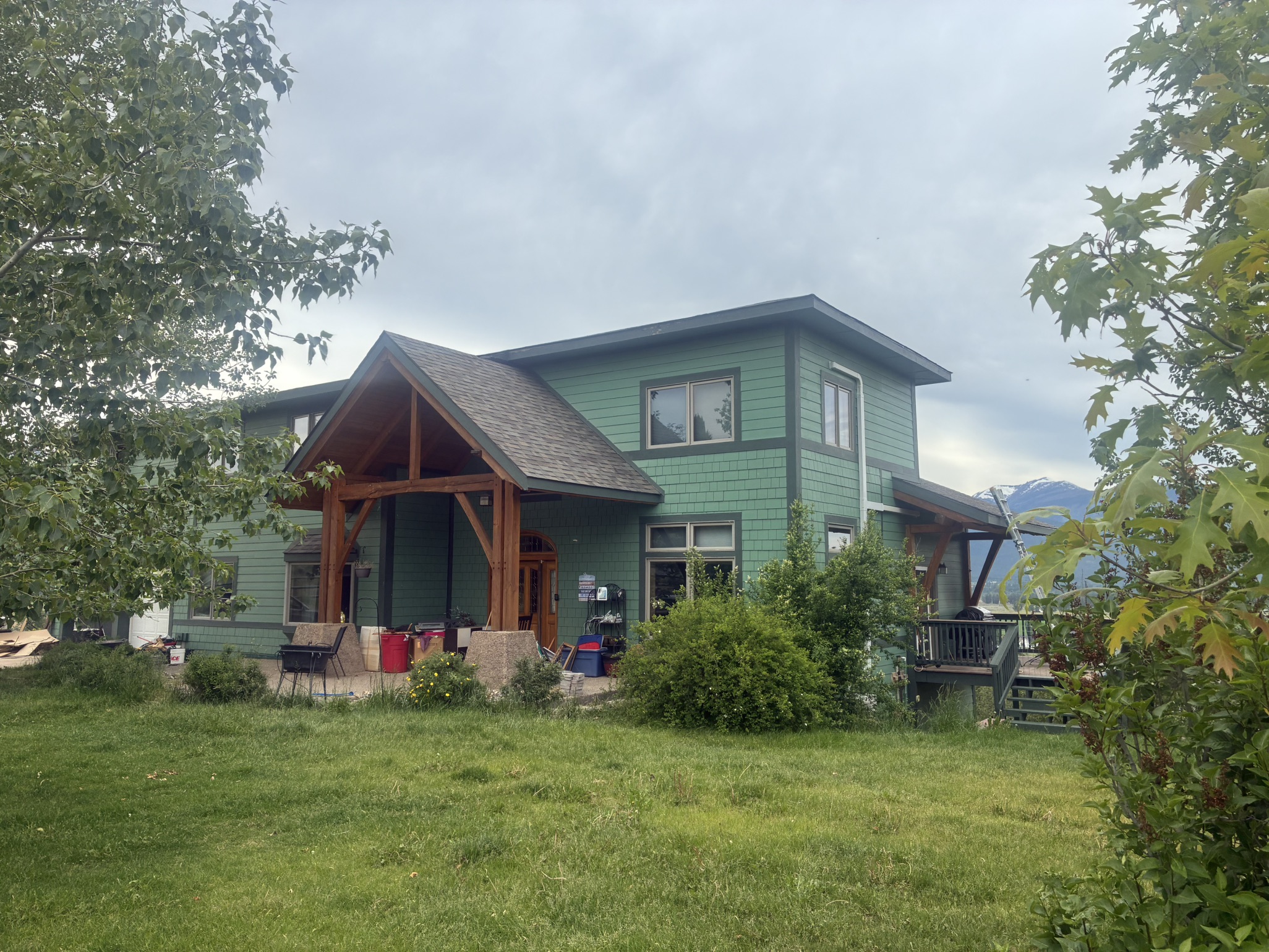 Green modern home with a timber-frame entry and mountain views.