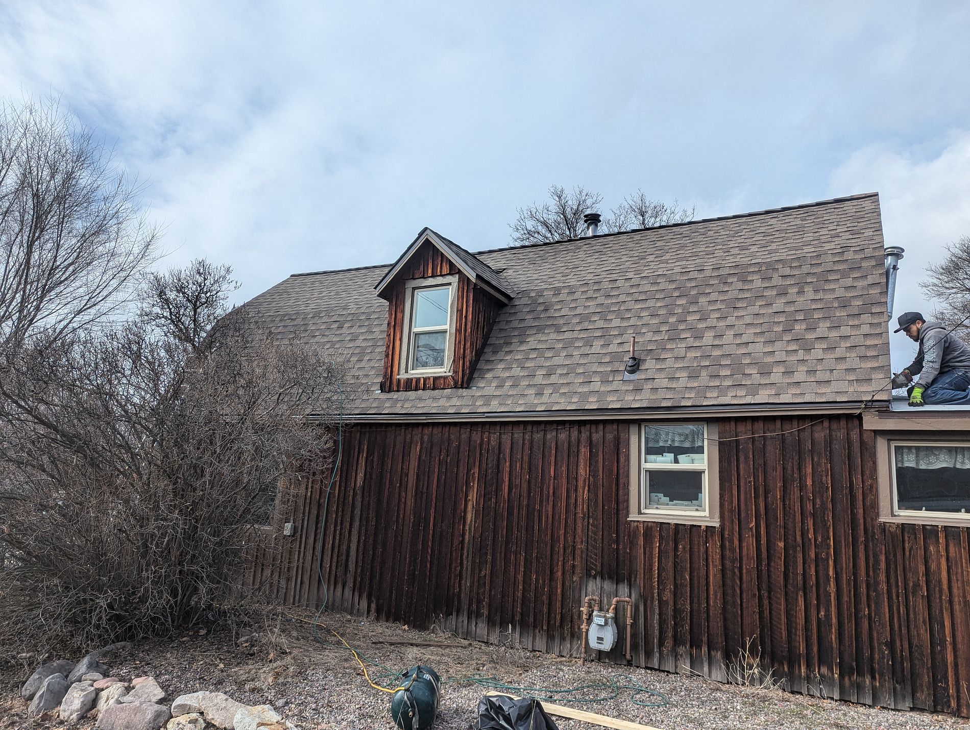 A roofer at the edge of a gambrel roof with freshly installed architectural shingles