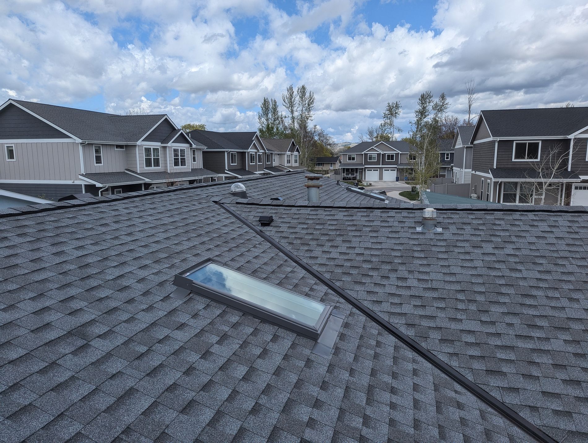 Charcoal architectural shingle roof with a skylight, overlooking a newer residential subdivision.