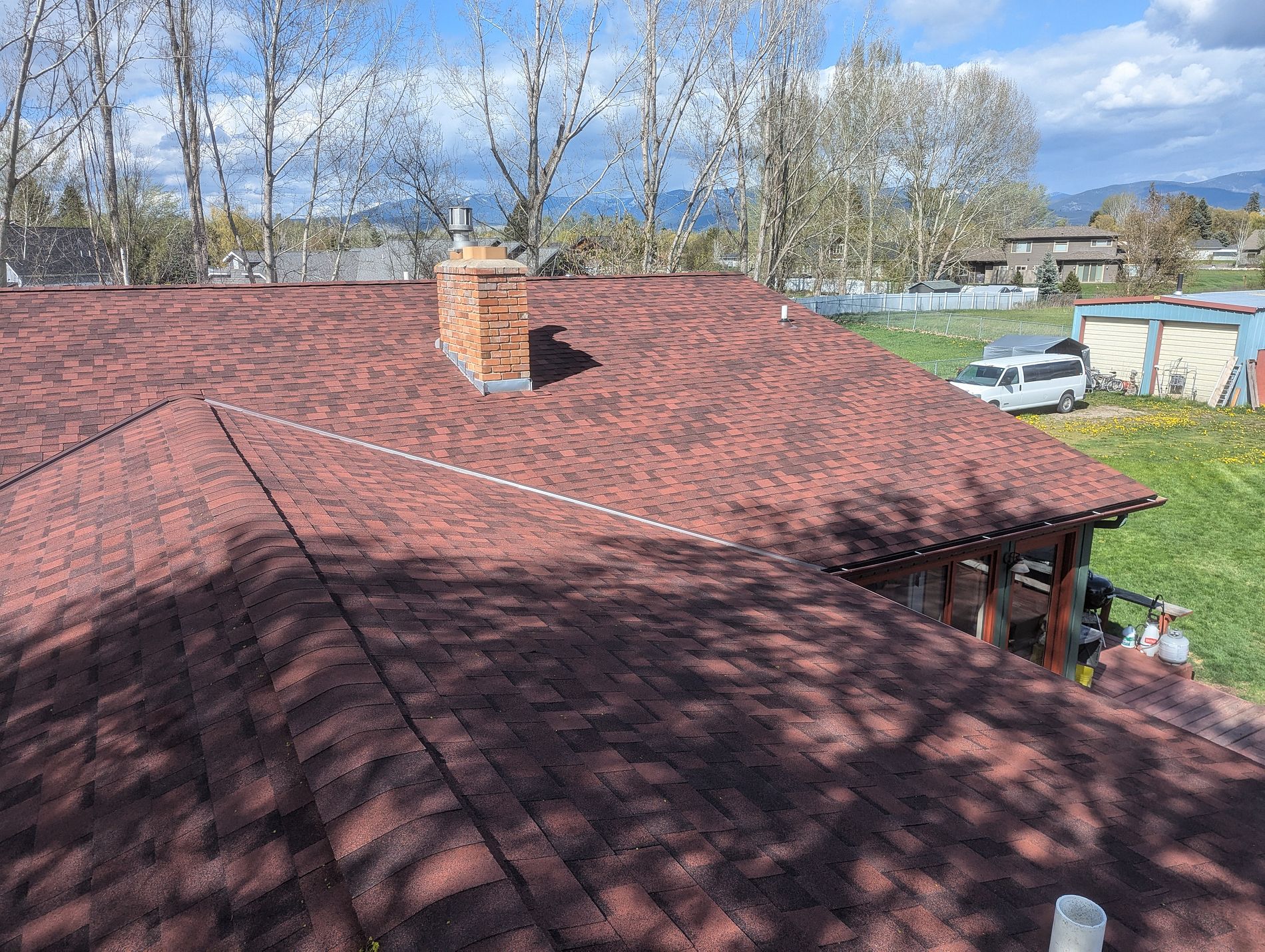 Aerial view of a red-toned shingle roof on a ranch home with a carport and green yard.