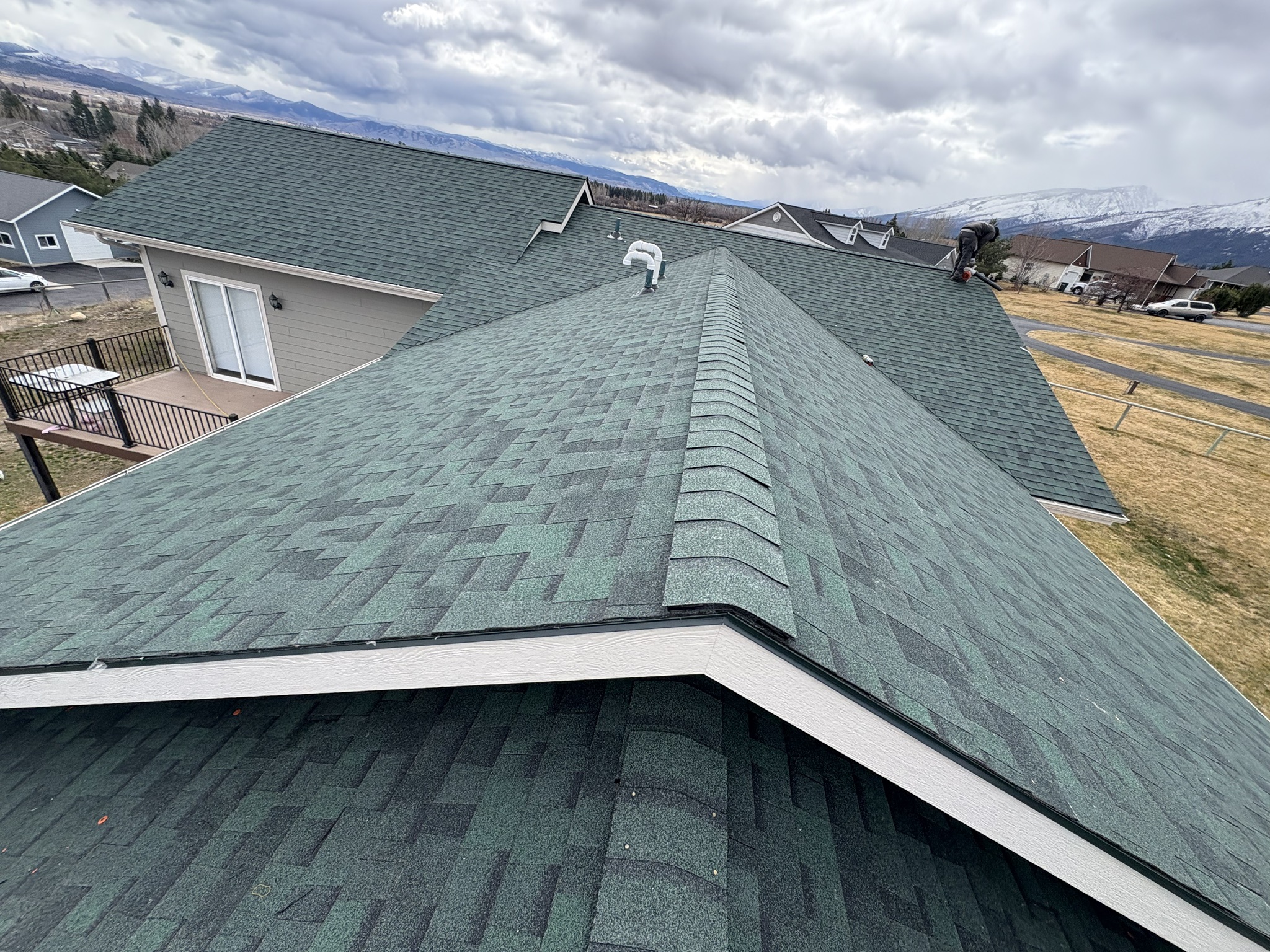 Older green shingle roof ridge with open fields beyond — before