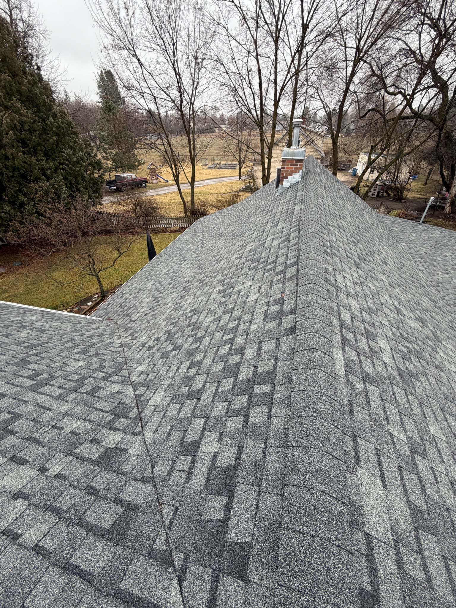 Steep gray shingle roof showing storm wear among bare trees — before