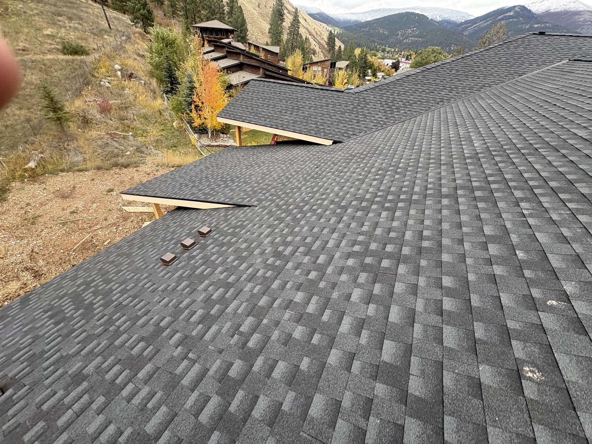 Close-up of a gray architectural shingle roof with a hillside town in the background.