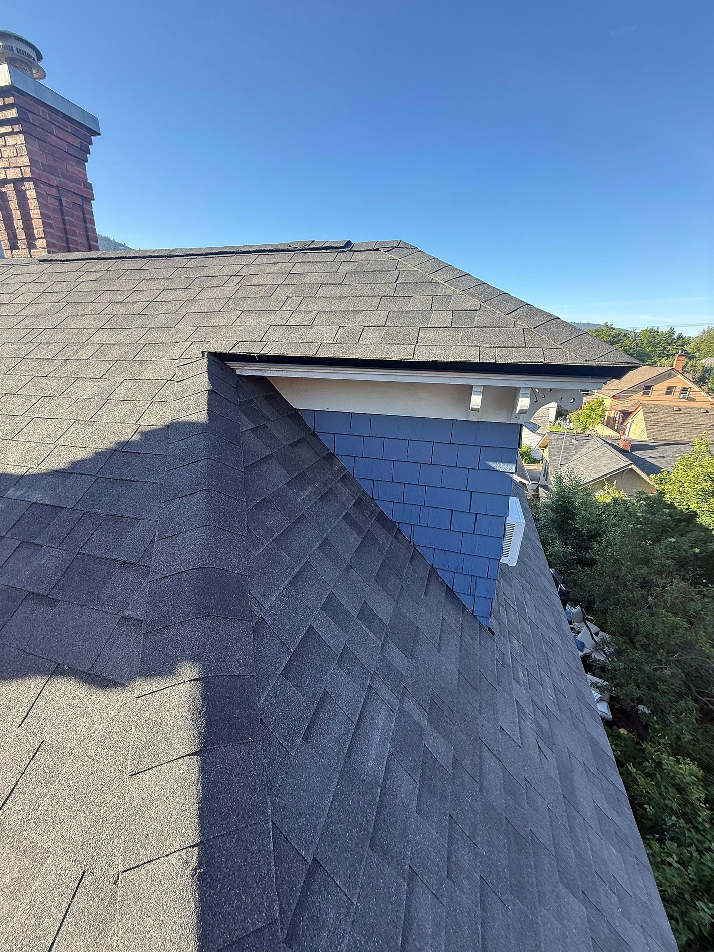 Gray architectural shingle roof with dormers under a clear blue sky.