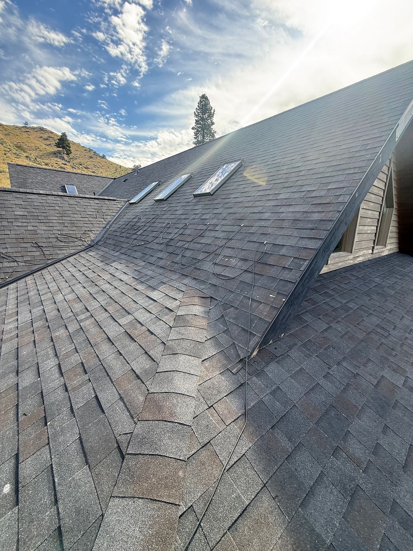 Gray architectural shingle roof with skylights and a hillside beyond.
